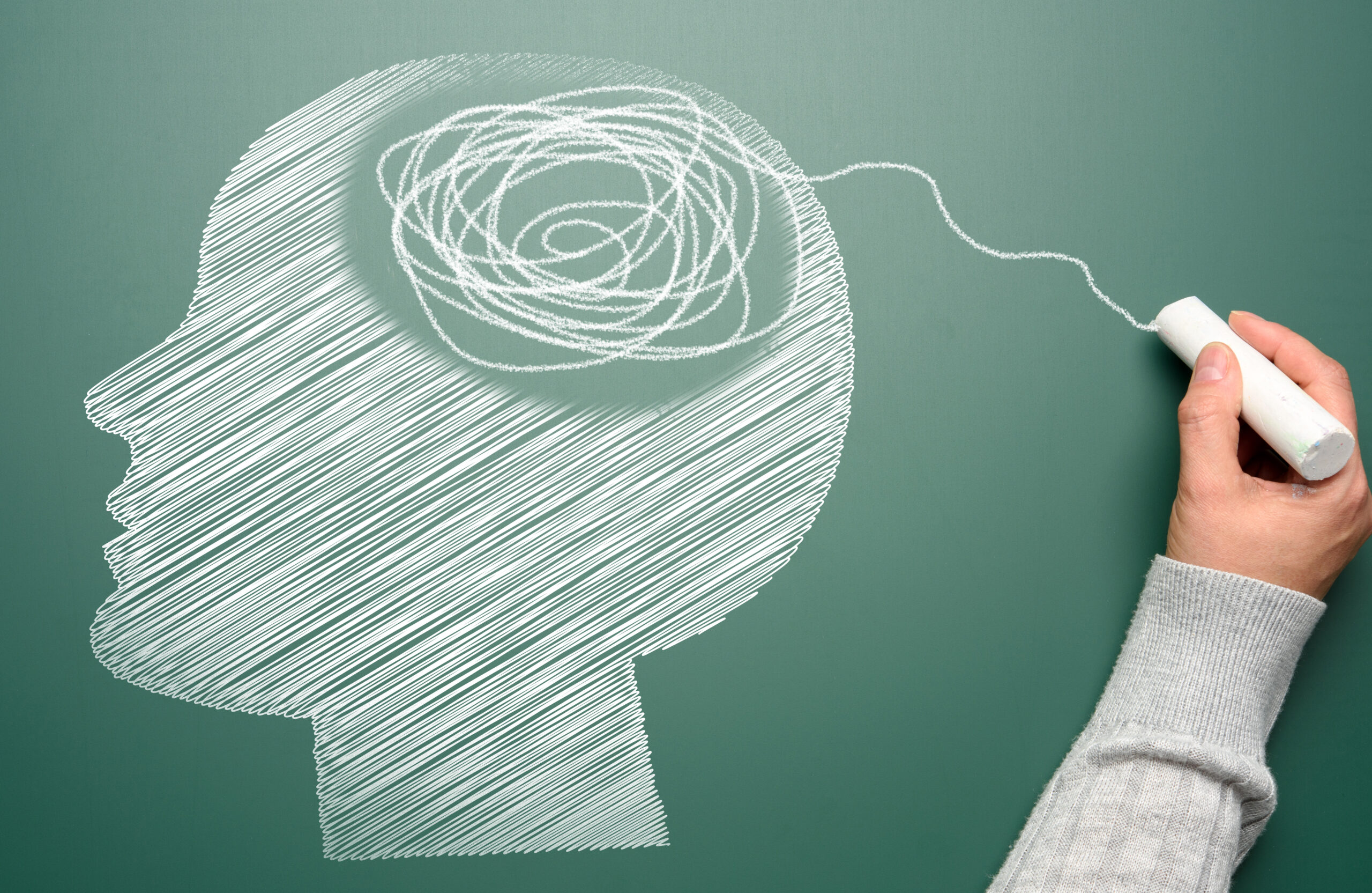 Profile of a human head with a tangled spiral in the brain area. The head is drawn in white chalk. Mental health concept
